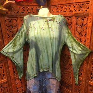 May include: A green tie-dye top with long, flared sleeves and a scoop neckline. The top is adorned with colorful sequins along the neckline and sleeve edges. Below, a pair of blue and gray patterned pants completes the ensemble, creating a bohemian look.