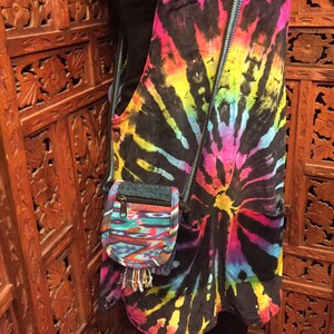 Pode incluir: Um vestido de macac&atilde;o tie-dye com uma pequena bolsa transversal tecida colorida. O vestido tem um fundo preto com redemoinhos tie-dye arco-&iacute;ris.