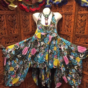May include: A black and white floral print dress with a high neckline and a layered skirt. The dress has a flowing, loose fit and is made of a lightweight fabric. The dress is accessorized with a turquoise and purple necklace.