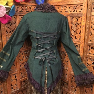 Könnte beinhalten: Eine dunkelgrüne Cordjacke mit Spitzenbesatz und einem Schnürrücken. Die Jacke hat einen hohen Kragen und lange Ärmel.