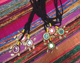 May include: A set of five black cord necklaces with colorful, mirrored pendants. Each pendant is surrounded by small white seashells and has a gold trim.