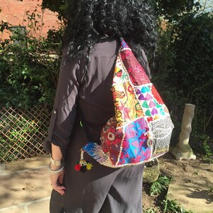 Könnte beinhalten: Eine bunte Patchwork-Tasche mit einem Quastenanhänger. Die Tasche besteht aus verschiedenen Stoffen und hat eine Vielzahl von Farben und Mustern. Die Tasche wird über der Schulter einer Person mit langen schwarzen Haaren getragen.