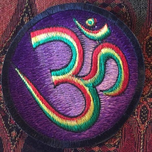 Peut inclure: Un patch brodé violet avec un symbole Om couleur arc-en-ciel.