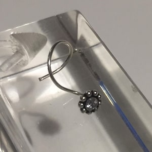 May include: A silver nose ring with a small, clear gemstone in the centre of a flower-shaped setting.