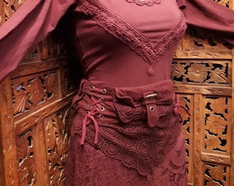 Pode incluir: Uma blusa de manga comprida vinho com detalhes em renda e uma saia vinho combinando com acabamento em renda. A saia tem um cinto de tecido castanho com fivela e atacadores.