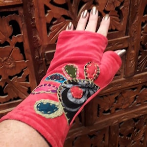 Op de afbeelding: Rode vingerloze handschoenen met kleurrijke geborduurde patches en een zwart-wit bloemenmotief.