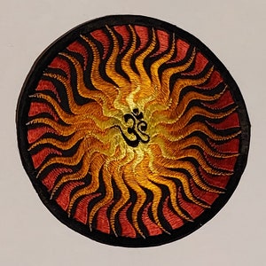 Peut inclure: Un écusson rond brodé avec une bordure noire et un motif de soleil éclatant rouge, orange et jaune. Le centre de l'écusson présente un symbole Om brodé en or.