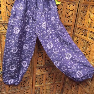 May include: Purple cotton pants with a white sun and moon print. The pants have an elastic waistband and a loose, flowing fit.