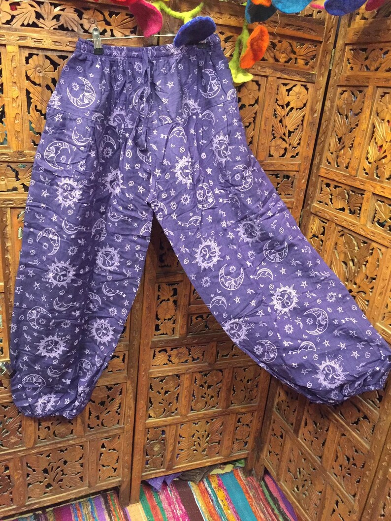 May include: Purple cotton pants with a white sun and moon print. The pants have an elastic waistband and a loose, flowing fit.