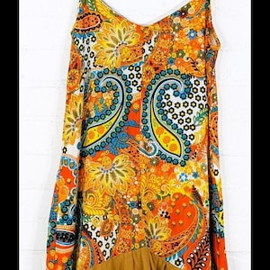 May include: A sleeveless, orange, yellow, blue, and white paisley print dress with a brown ruffle hem. The dress has a V-neckline and thin straps.