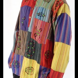May include: A multi-coloured patchwork shirt with long sleeves and a button-up collar. The shirt is made of striped fabric in various colours, including red, yellow, blue, green, and brown. The shirt features embroidered designs in black and green.