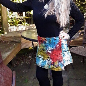 Könnte beinhalten: Eine Frau trägt ein schwarzes Langarmhemd mit einer silbernen Halskette und einen bunten Batikrock mit einem Pilz-Druck. Sie steht in einem Garten.