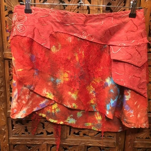 May include: A red, multi-layered skirt with a tie-dye pattern and a decorative embroidered trim. The skirt has a frayed hem and a pocket on the side.