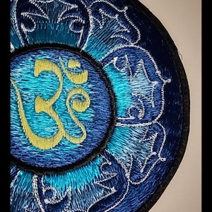 Peut inclure: Écusson brodé avec un motif détaillé dans les tons de bleu et de turquoise, et un symbole Om doré au centre. L'écusson a une bordure noire et des accents blancs. L'URL de la boutique Etsy est visible en bas.