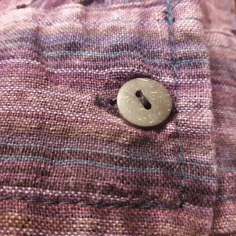 Op de afbeelding: Een close-up van een bruine, ronde kokosnootknoop die op een paars-blauwe gestreepte stof is genaaid.