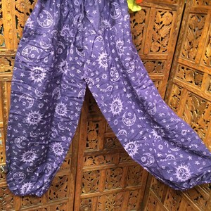 May include: Purple cotton pants with a white sun and moon print. The pants have an elastic waistband and a drawstring.