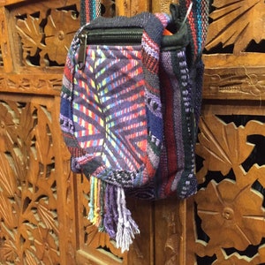 Pode incluir: Uma pequena bolsa transversal tecida colorida com fecho de correr e um tassel. A bolsa &eacute; feita de uma variedade de tecidos e tem um padr&atilde;o geom&eacute;trico.
