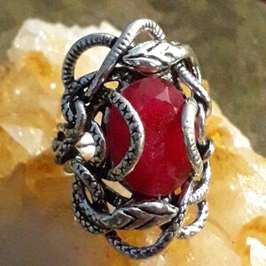 May include: A silver ring with a red gemstone set in a snake and leaf design.