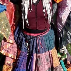 May include: A colorful patchwork skirt with multiple tiers in shades of blue, purple, green, and orange. The skirt is paired with a burgundy top and a matching head covering, creating a bohemian style.