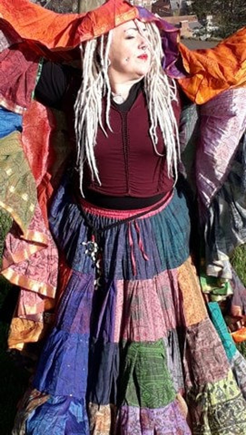 May include: A colorful patchwork skirt with multiple tiers in shades of blue, purple, green, and orange. The skirt is paired with a burgundy top and a matching head covering, creating a bohemian style.