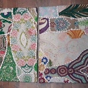 May include: Two square patchwork throw pillows with a variety of colorful fabrics and embellishments. The pillows are made of a beige fabric with different colored patches sewn on top. The patches are made of different fabrics, including velvet, satin, and brocade. The pillows are decorated with beads, sequins, and embroidery.