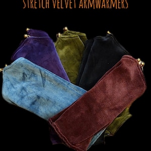 Puede incluir: Colección de calentadores de brazo de terciopelo elástico en varios colores: azul, morado, verde oliva, negro y burdeos. Cada calentador de brazo tiene un detalle dorado. El texto de la imagen dice "NEW COLLECTION STRETCH VELVET ARM WARMERS."