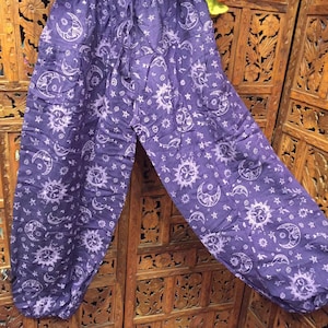 May include: Purple cotton pants with a white sun and moon print. The pants have an elastic waistband and a loose, flowing fit.