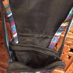 Pode incluir: Uma pequena bolsa preta com z&iacute;per e uma al&ccedil;a estampada colorida. A bolsa &eacute; feita de um tecido preto macio e tem um fecho de z&iacute;per. A al&ccedil;a &eacute; feita de um tecido tecido com uma variedade de cores, incluindo azul, vermelho e branco.
