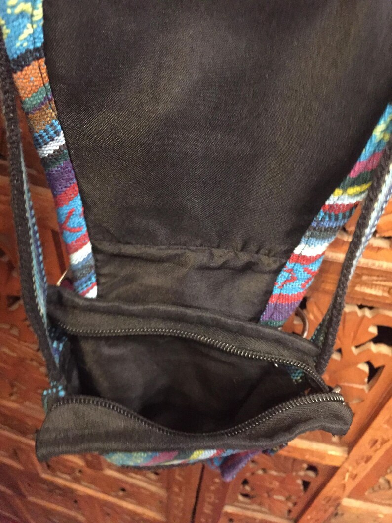 Pode incluir: Uma pequena bolsa preta com z&iacute;per e uma al&ccedil;a estampada colorida. A bolsa &eacute; feita de um tecido preto macio e tem um fecho de z&iacute;per. A al&ccedil;a &eacute; feita de um tecido tecido com uma variedade de cores, incluindo azul, vermelho e branco.