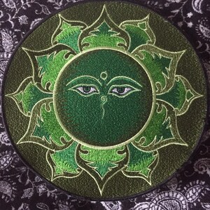 May include: Green embroidered patch with a stylized eye design in the center, surrounded by a circular floral pattern.