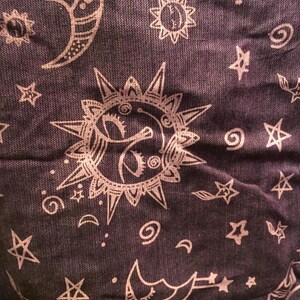 May include: A dark purple fabric with a white repeating pattern of stars, moons, and suns. The pattern is a whimsical and celestial design.