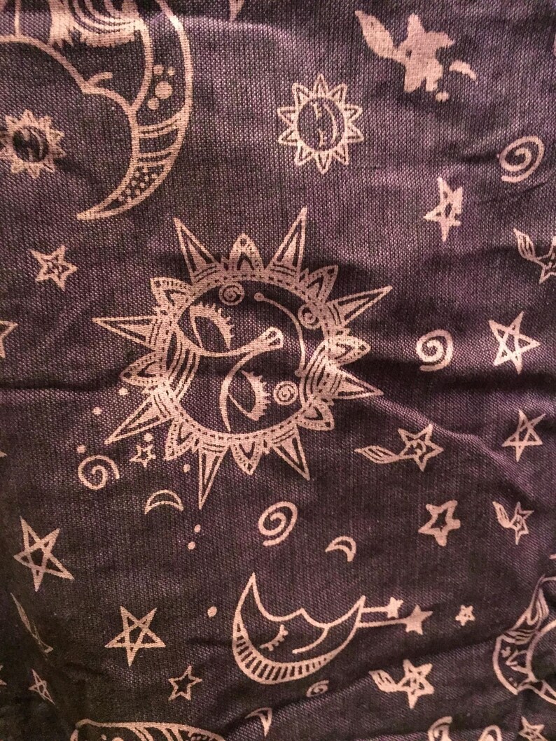 May include: A dark purple fabric with a white repeating pattern of stars, moons, and suns. The pattern is a whimsical and celestial design.