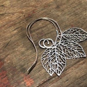 May include: Silver leaf earrings with a delicate wire design. The earrings are shaped like leaves with intricate details.