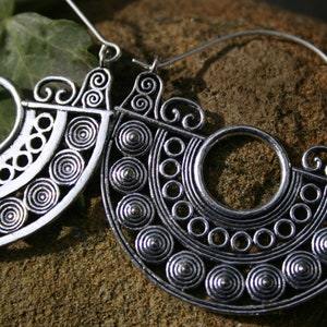 May include: A pair of silver hoop earrings with a circular design featuring intricate swirls and concentric circles.
