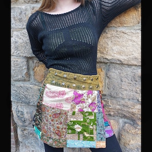 Peut inclure: Une jupe en patchwork avec une variété de tissus et de motifs colorés. La jupe a une ceinture en cuir marron avec des clous métalliques et un pull en maille noir est porté par-dessus la jupe.