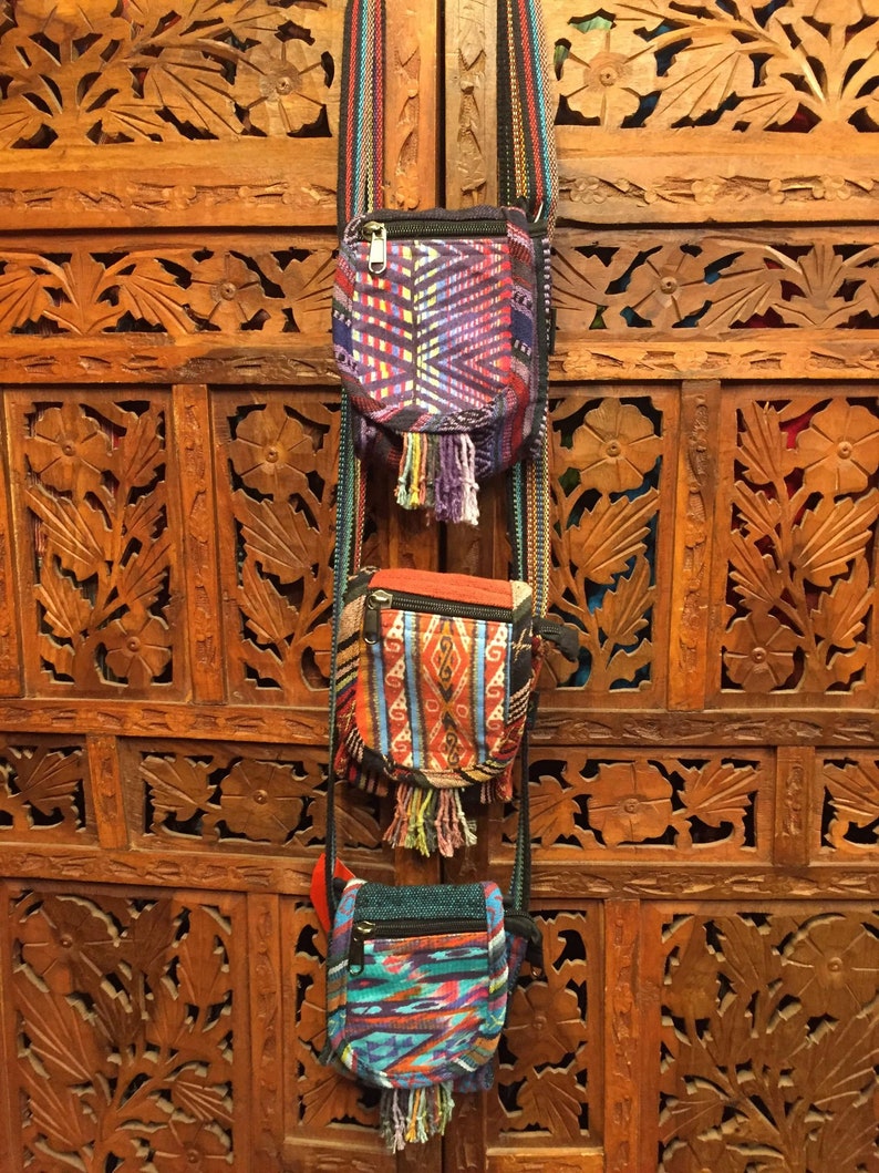 Pode incluir: Tr&ecirc;s pequenas bolsas coloridas e estampadas com franjas penduradas na parte inferior. As bolsas est&atilde;o presas a al&ccedil;as longas e est&atilde;o penduradas em uma parede de madeira.