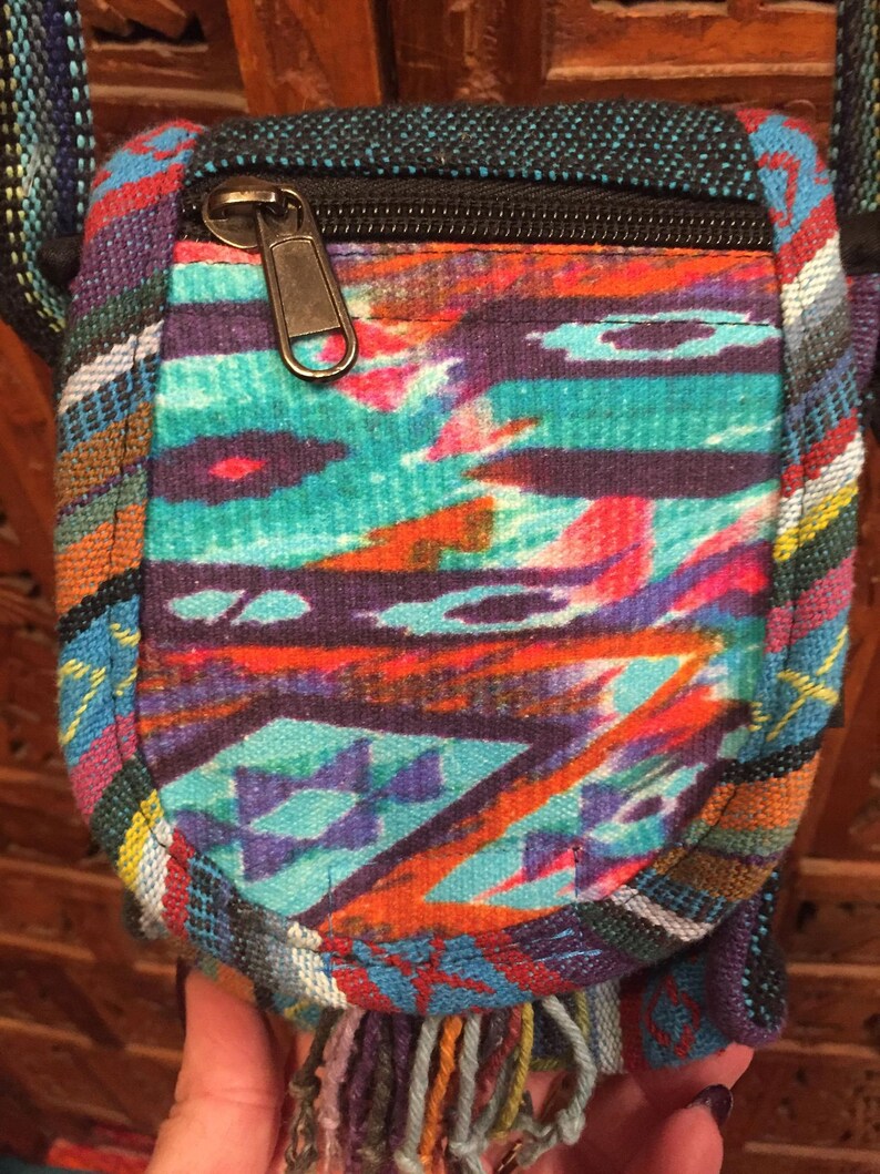 Pode incluir: Uma pequena bolsa transversal tecida colorida com fecho de correr e um tassel de franjas. A bolsa &eacute; feita de uma variedade de tecidos e tem um padr&atilde;o geom&eacute;trico.