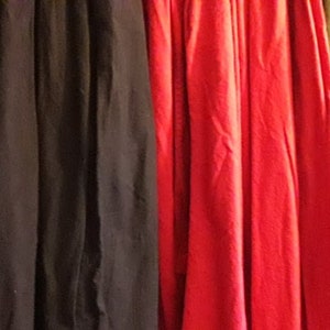 May include: A close-up of several vertical fabric panels in various colors. The colors include teal, black, red, and olive green. The fabric appears to be draped, with visible folds and textures.