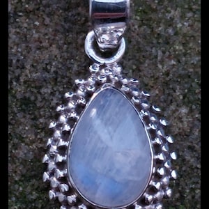 Puede incluir: Colgante de plata con una piedra lunar azul claro en forma de pera. La piedra está engastada en un marco de plata texturizado y con cuentas. El colgante tiene una argolla de plata para una cadena. www.gutsygingers.etsy.com.