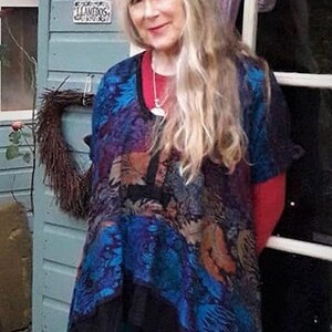 Puede incluir: Una mujer con el pelo largo y rubio lleva una chalina con estampado azul y negro con una camiseta roja debajo. Lleva leggings azul oscuro y botas negras. La mujer está de pie frente a una puerta blanca con un cartel que dice "Limnos Grecia".