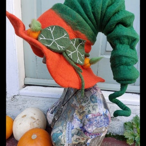 Peut inclure: Un chapeau fantaisiste en feutre orange et vert avec un dessus vert en spirale. Le chapeau présente des feuilles en feutre avec des coutures blanches et de petits accents de citrouille orange. Le chapeau est exposé sur une tête de mannequin avec des citrouilles au premier plan.