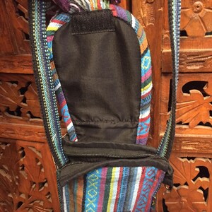 Pode incluir: Uma pequena bolsa transversal listrada colorida com um z&iacute;per preto e uma al&ccedil;a preta. A bolsa est&aacute; aberta e o interior &eacute; forrado com tecido preto.