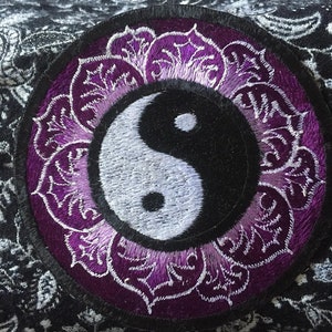 Peut inclure: Un symbole yin yang brodé en violet et blanc avec un motif de mandala autour. Le patch est circulaire et a une bordure noire.