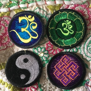 Peut inclure: Quatre patchs brodés avec des symboles spirituels. Les patchs sont circulaires et présentent un symbole Om bleu, un symbole Om vert dans une fleur de lotus, un symbole yin yang noir et blanc et un symbole de nœud sans fin violet.