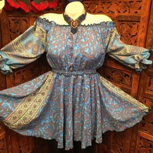 Op de afbeelding: Een blauwe en paarse off-shoulder jurk met een paisley-patroon. De jurk heeft een getailleerde taille en 3/4 mouwen.