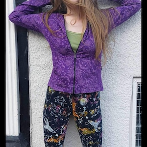 May include: A purple zip-up hoodie with a white celestial print. The model is wearing black leggings with a white celestial print.