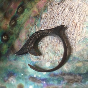 May include: A black metal ring with a leaf design. The ring is on a iridescent background.