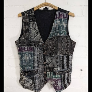 May include: A black and gray patchwork vest with a variety of patterns, including suns, stars, and geometric designs. The vest has a V-neck and five buttons down the front.