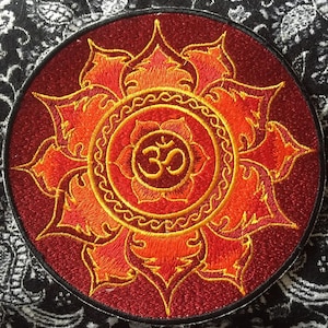 Peut inclure: Un patch brodé rouge et or avec un symbole Om au centre entouré d'un motif de fleur stylisé.