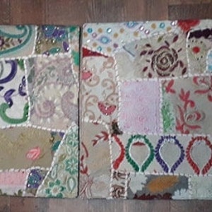 May include: Two square patchwork throw pillows with a cream background and colorful fabric scraps sewn together. The pillows feature a variety of patterns and textures, including paisley, floral, and geometric designs. The pillows are embellished with beads and sequins.